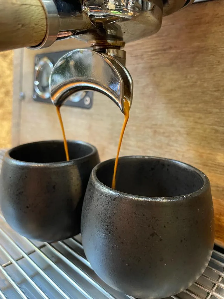 Dos espressos cayendo del portafiltro en dos tazas negras de Boconó