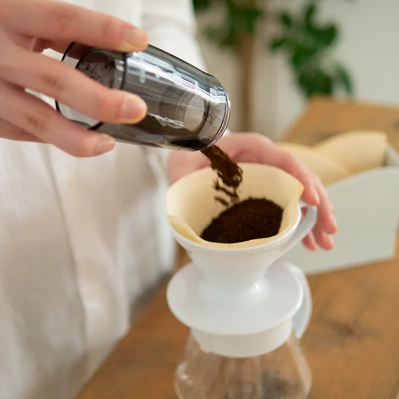 El depósito del molinillo vierte el café recién molido dentro de un filtro V60 colocado sobre una jarra.