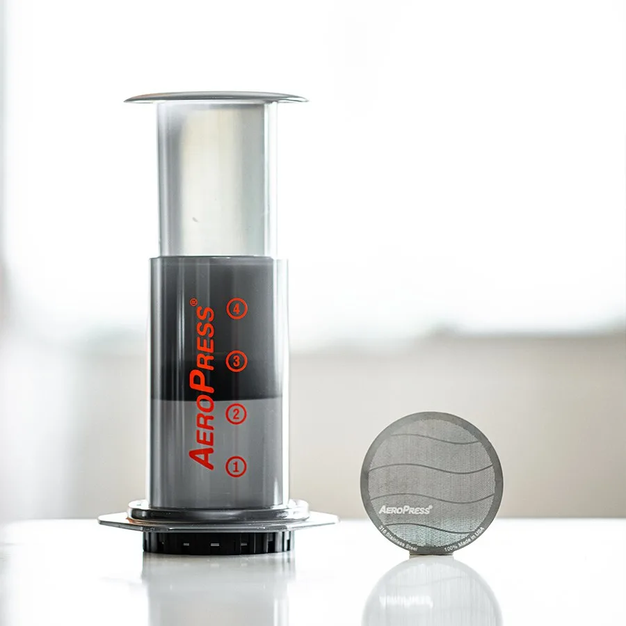 Filtro metálico estándar AeroPress al lado de la cámara de la cafetera
