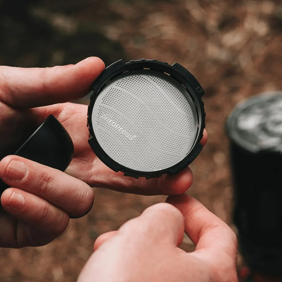 Unas manos colocan el filtro metálico estándar AeroPress dentro de la tapa
