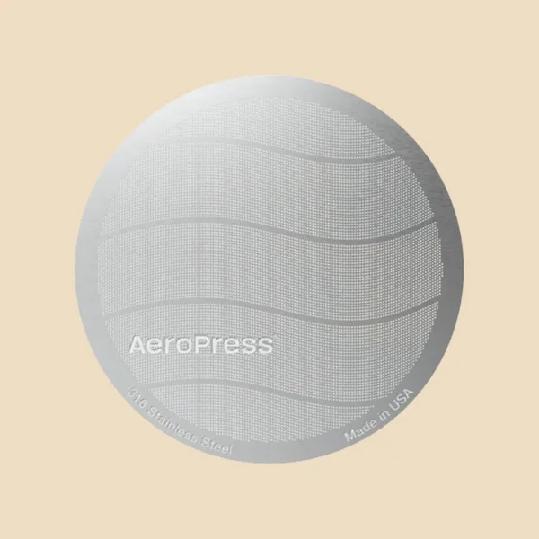 Filtro metálico estándar AeroPress visto de frente sobre fondo arena