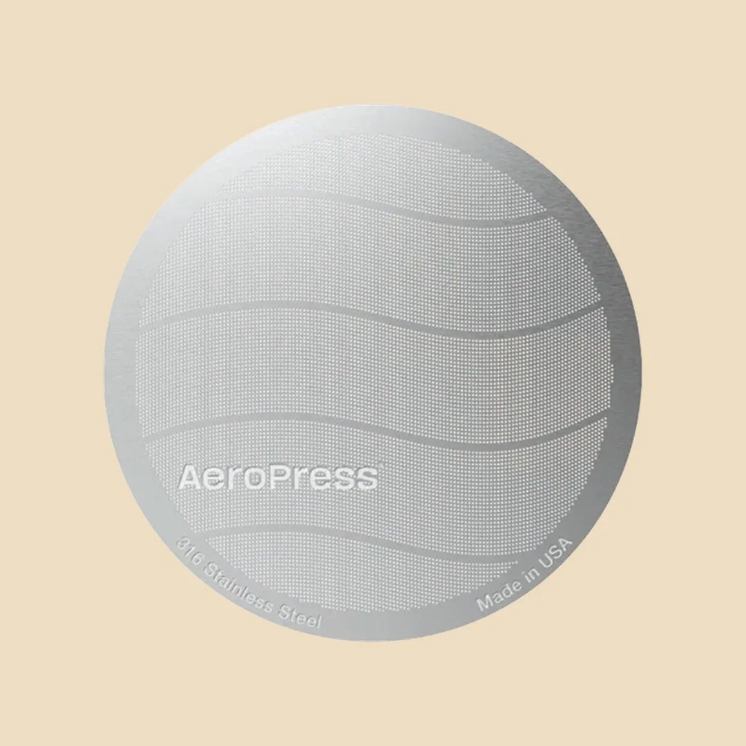 Filtro metálico estándar AeroPress visto de frente sobre fondo arena