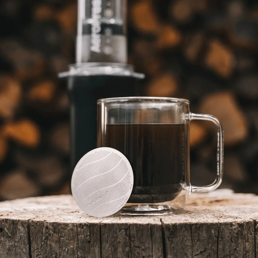 Filtro metálico estándar AeroPress junto a una taza de café preparado