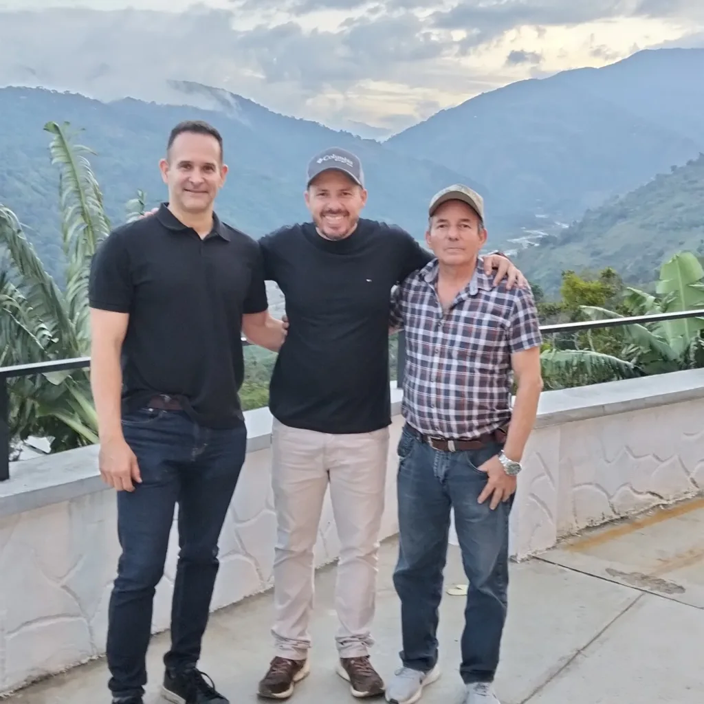 Andrés Román, en la terraza de su finca en Boconó (Trujillo, Venezuela), con su padre y Carlos Núñez, y las montañas de los Andes al fondo