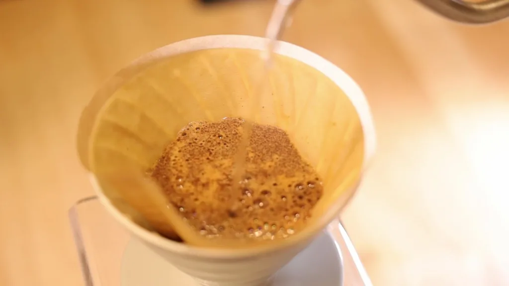 Café en floración dentro de un V60 blanco con filtro de papel, en la barra de Boconó