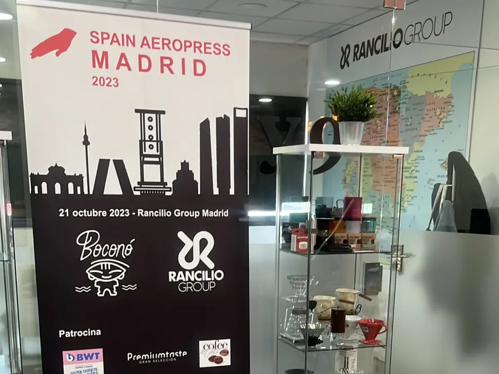 Roll-up del Spain AeroPress Madrid 2023 junto a una vitrina con cafeteras.