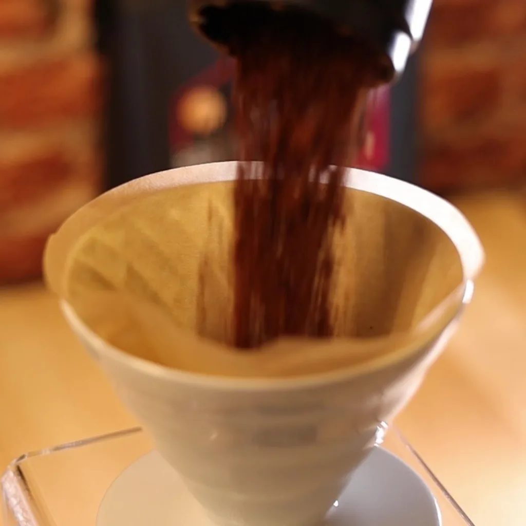 Café molido cayendo en el Hario V60 02 blanco con un filtro sin blanquear en Boconó