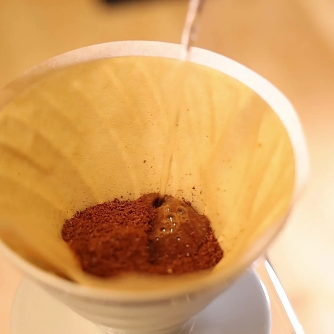 Primer chorro de agua sobre el café dentro del Hario V60 02 blanco