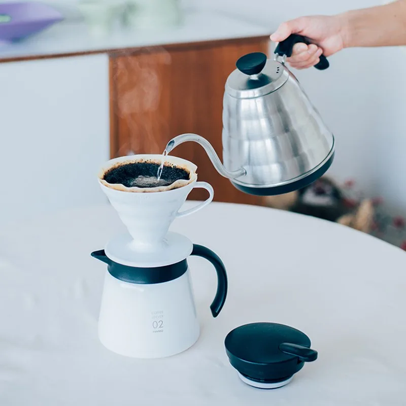 Hario V60 02 blanco sobre una jarra mientras recibe agua de un hervidor de cuello de cisne