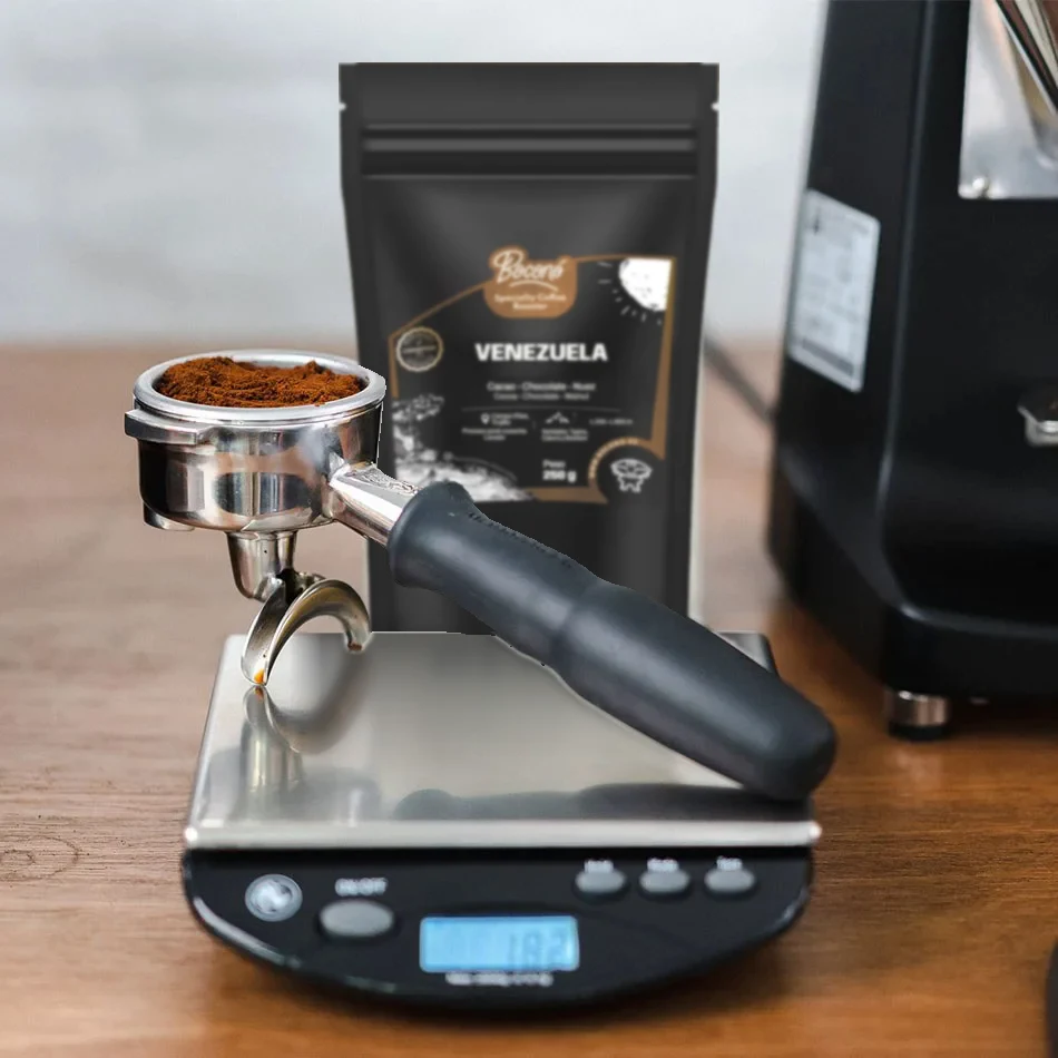 Rhino Bench Scale RCGPORT2KG con un portafiltros lleno de café molido, una bolsa de café de Venezuela de Boconó detrás y el molinillo al fondo