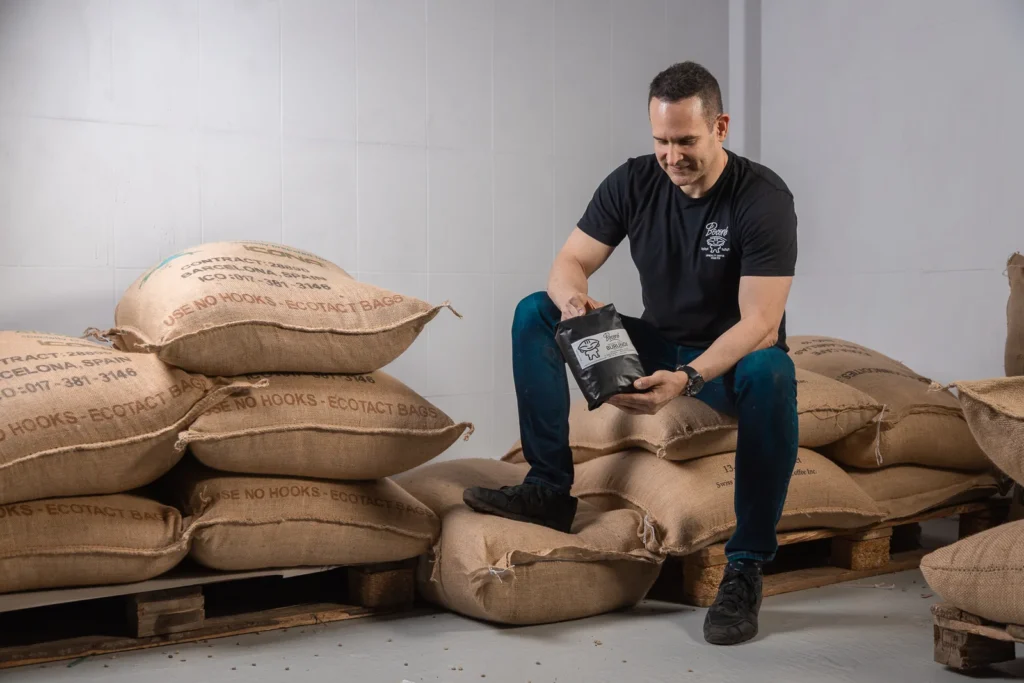 Una bolsa de café de Boconó en las manos, sobre sacos de yute de café verde, en el tostadero de Madrid