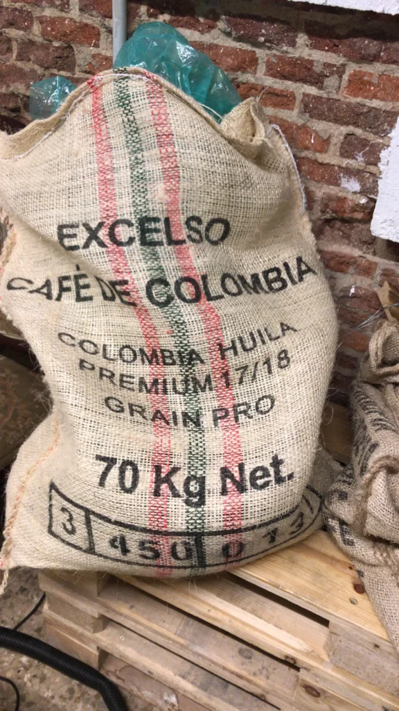 Saco de yute de 70 kilos de café verde «Excelso Café de Colombia, Colombia Huila Premium 17/18», sobre un palé junto a la pared de ladrillo del tostadero de Boconó, en abril de 2018