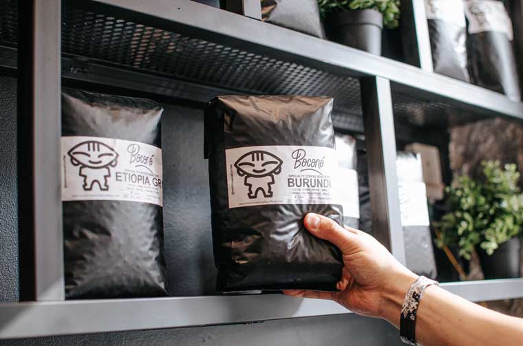 Mano cogiendo de la estantería una bolsa de café de especialidad de Boconó de Burundi, junto a otra de Etiopía