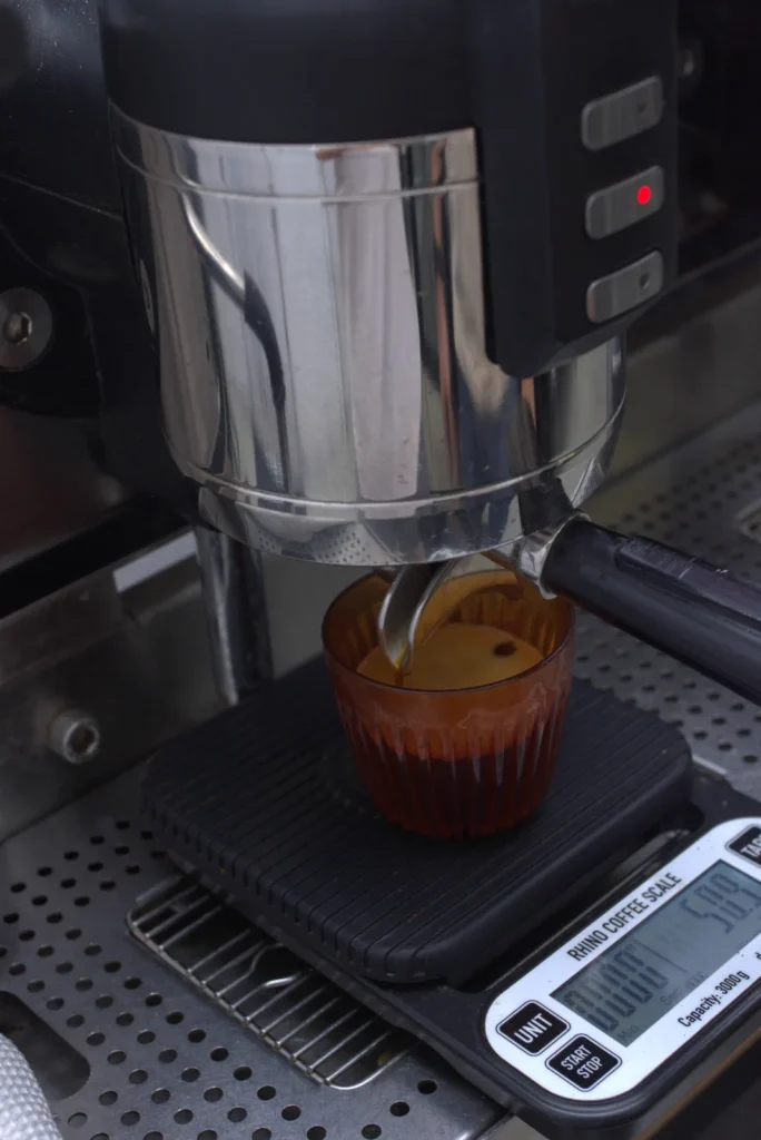 Un espresso cae del portafiltros en un vaso ámbar sobre la báscula, con la crema formándose arriba