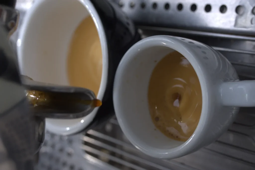 Las últimas gotas de un espresso caen del portafiltros en una taza blanca, sobre la crema que se está formando