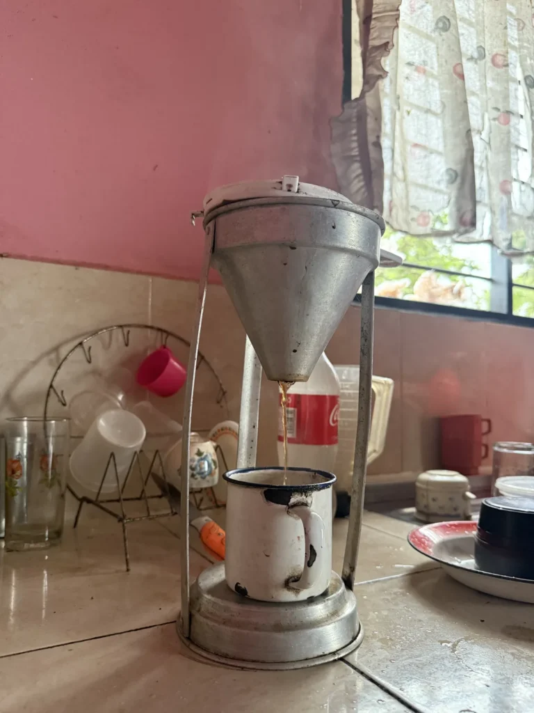 Coladora de café de aluminio colando sobre una taza de peltre en la cocina de la finca La Mesa de Palmarito, Zea