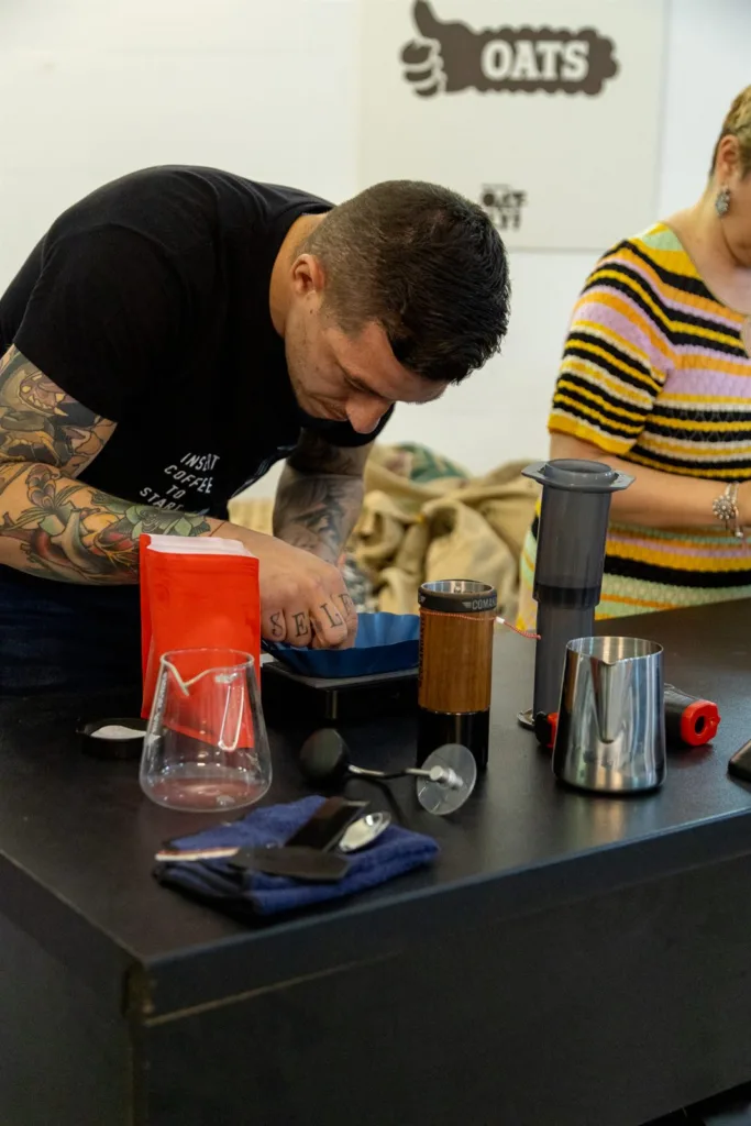 Competidor inclinado sobre la mesa preparando el café molido, con un molinillo manual y una AeroPress sobre la báscula