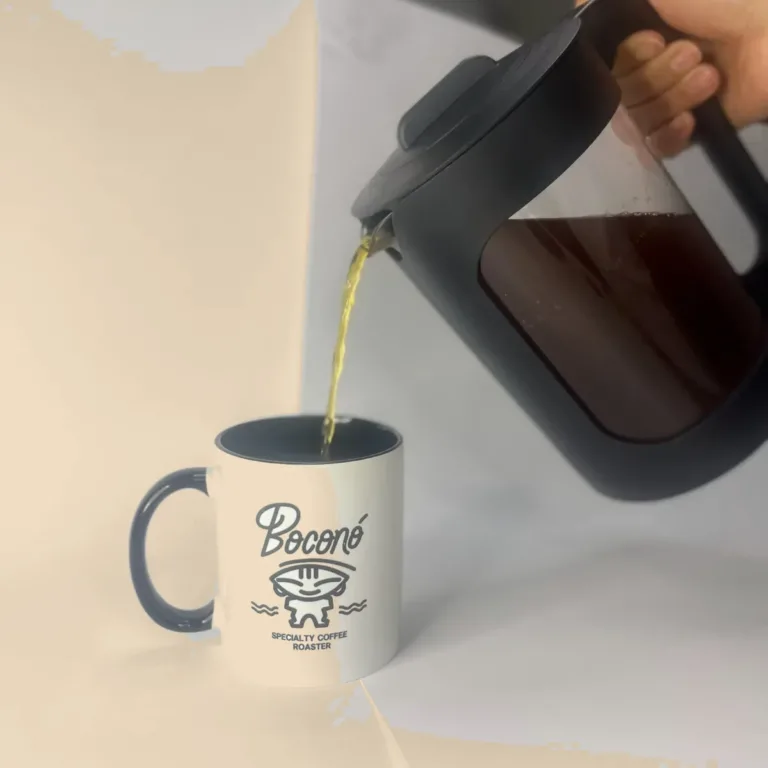 Una mano sirve cold brew desde la jarra negra de 1,5 litros de Boconó en una taza blanca con el logotipo de Boconó, sobre fondo blanco