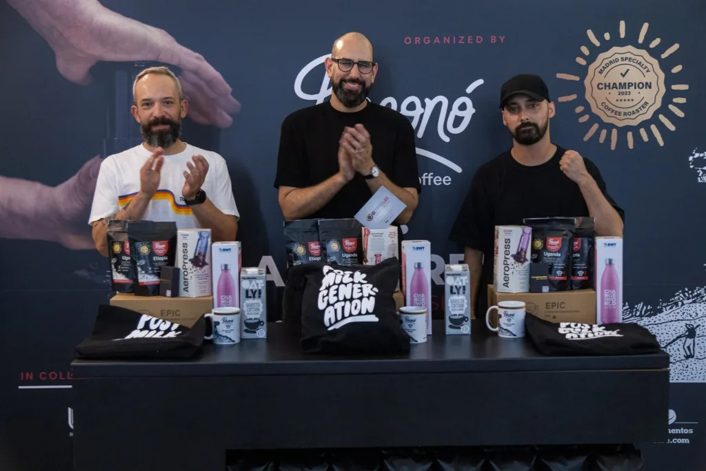 Los tres clasificados aplaudiendo detrás de la mesa con los premios, delante del photocall