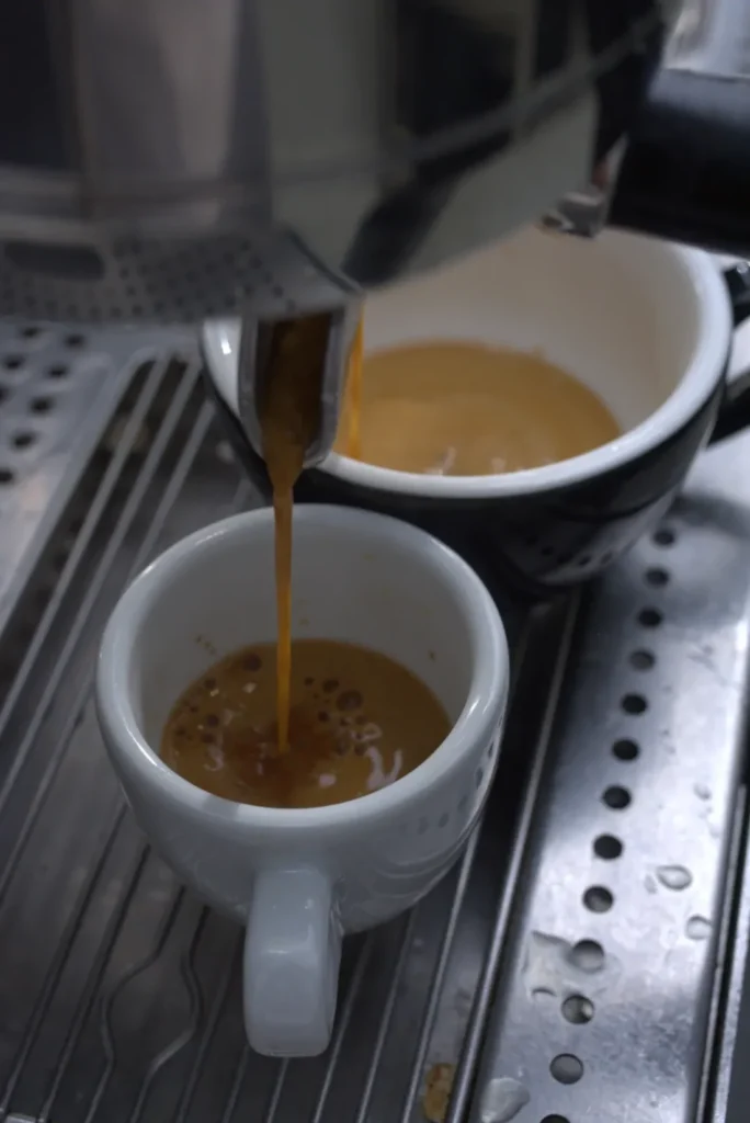 Un espresso cae del portafiltros a una taza blanca sobre la bandeja de la máquina