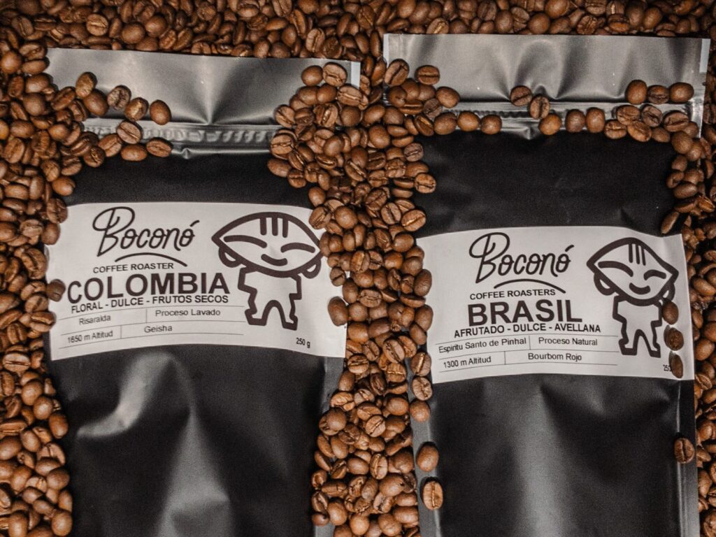 Etiquetas de dos bolsas de café de Boconó sobre grano tostado: Colombia Geisha lavado de Risaralda y Brasil Bourbon Rojo natural, con altitud y notas de cata